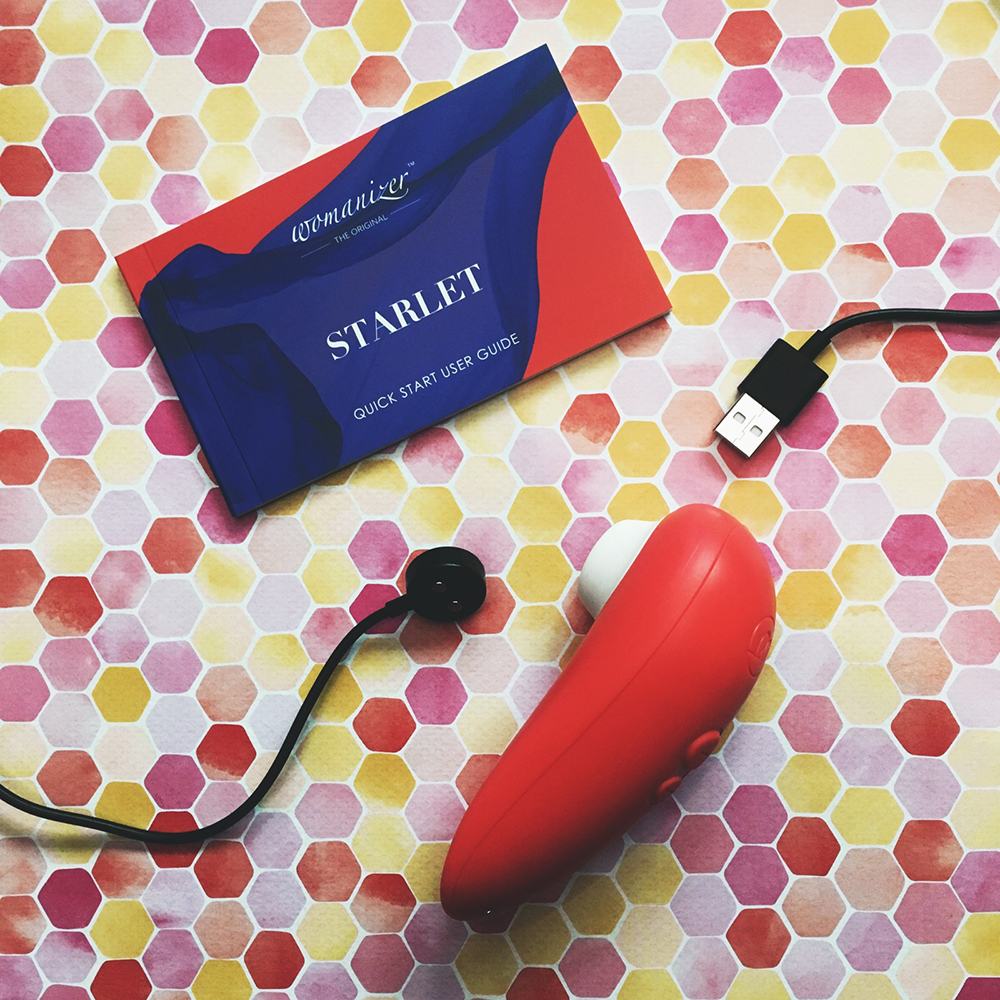 Photo of peach oval shaped Starlet 2 on its side, next to instruction book and charging cable