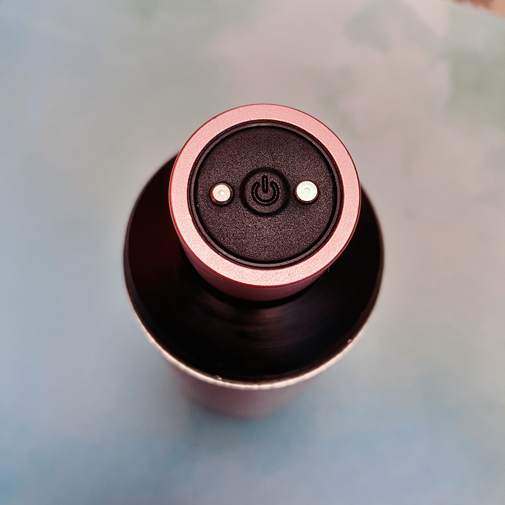 Top down view of bullet inside cylinder package, single black power button on end is visible between the magnet charger contacts