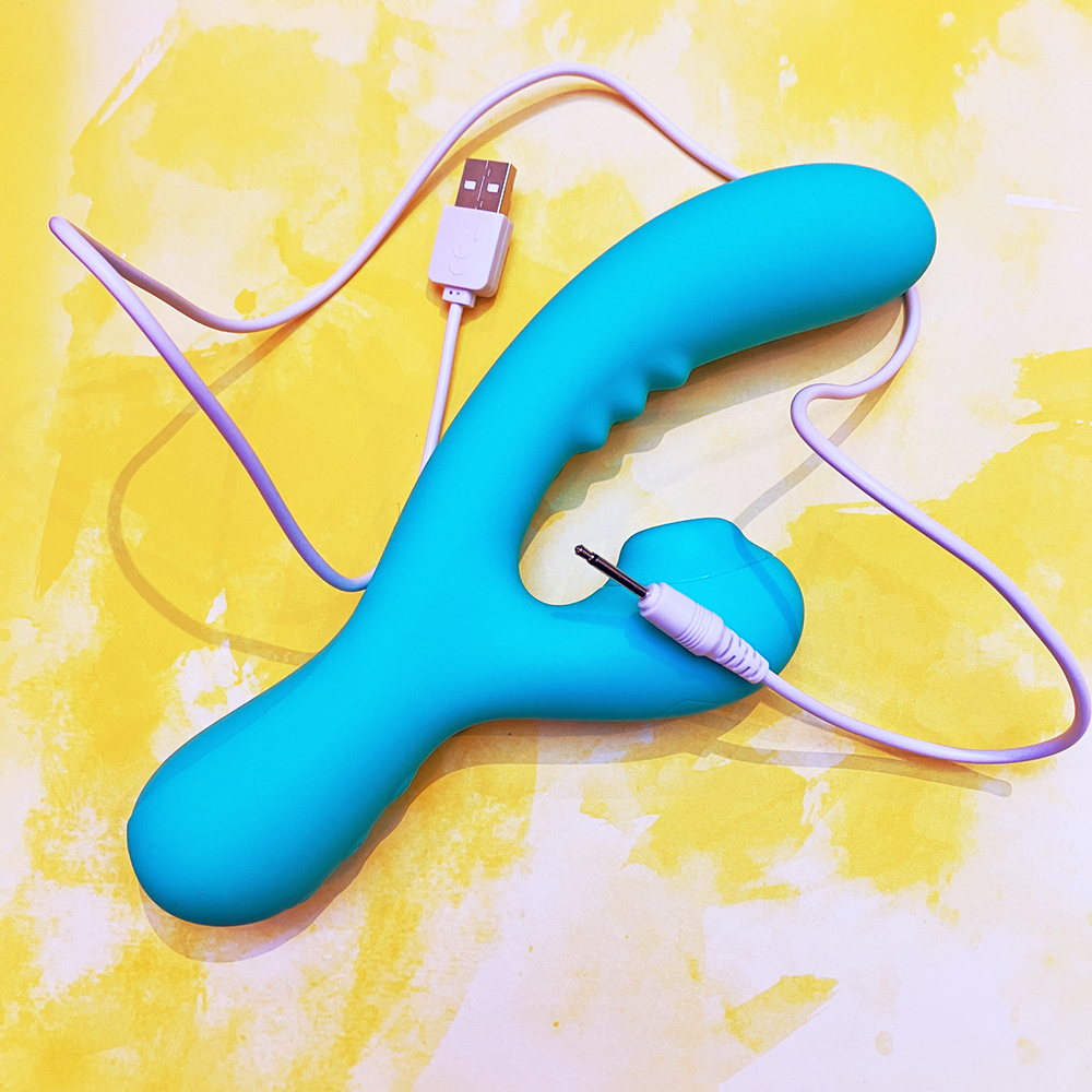 turquoise vibrator on yellow background, white USB charging cable draped across it
