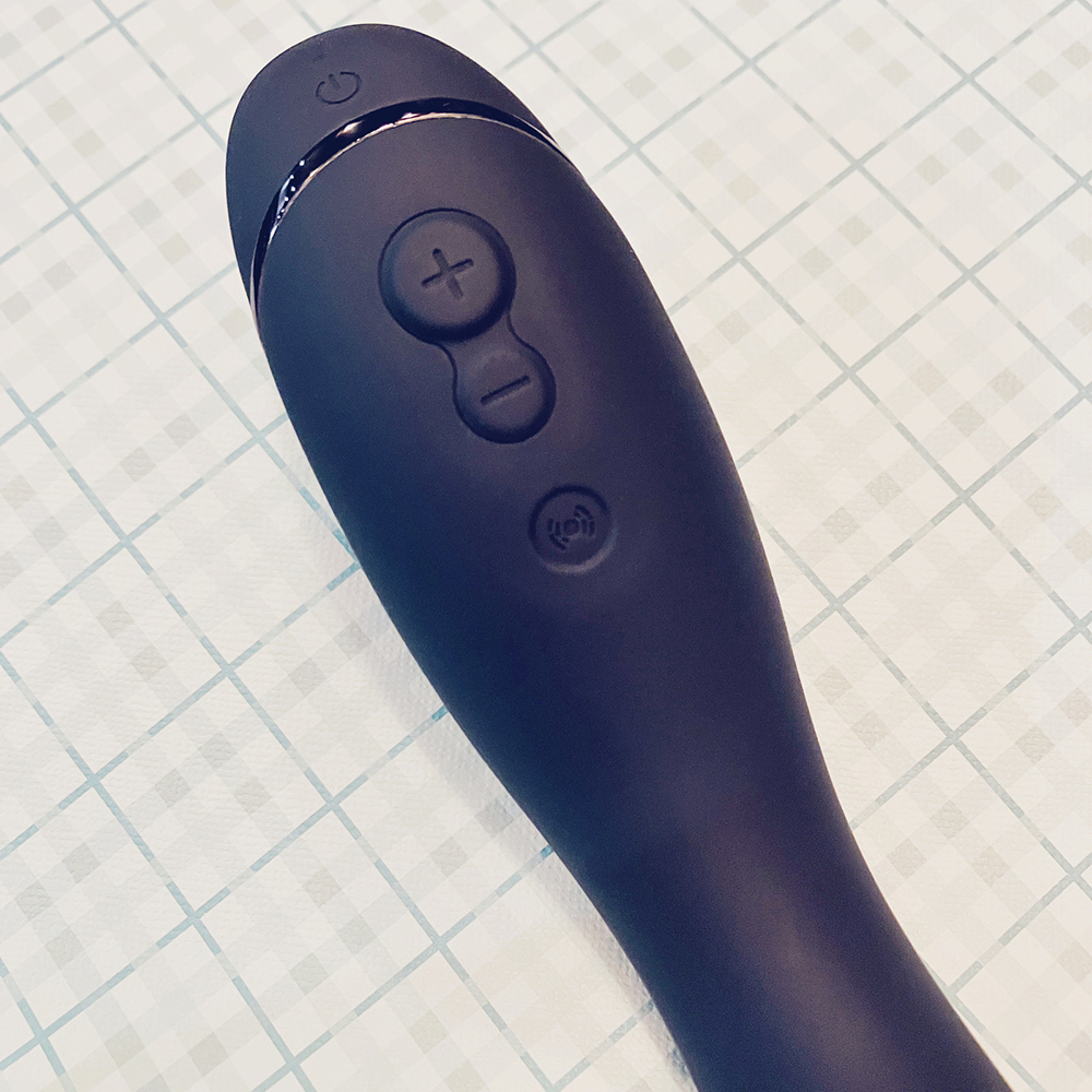 Photograph of handle of slate grey air-pulse toy showing buttons - power button at the very tip, then large plus sign button, then smaller minus sign button connected together, when a fourth vibration button a space below 
