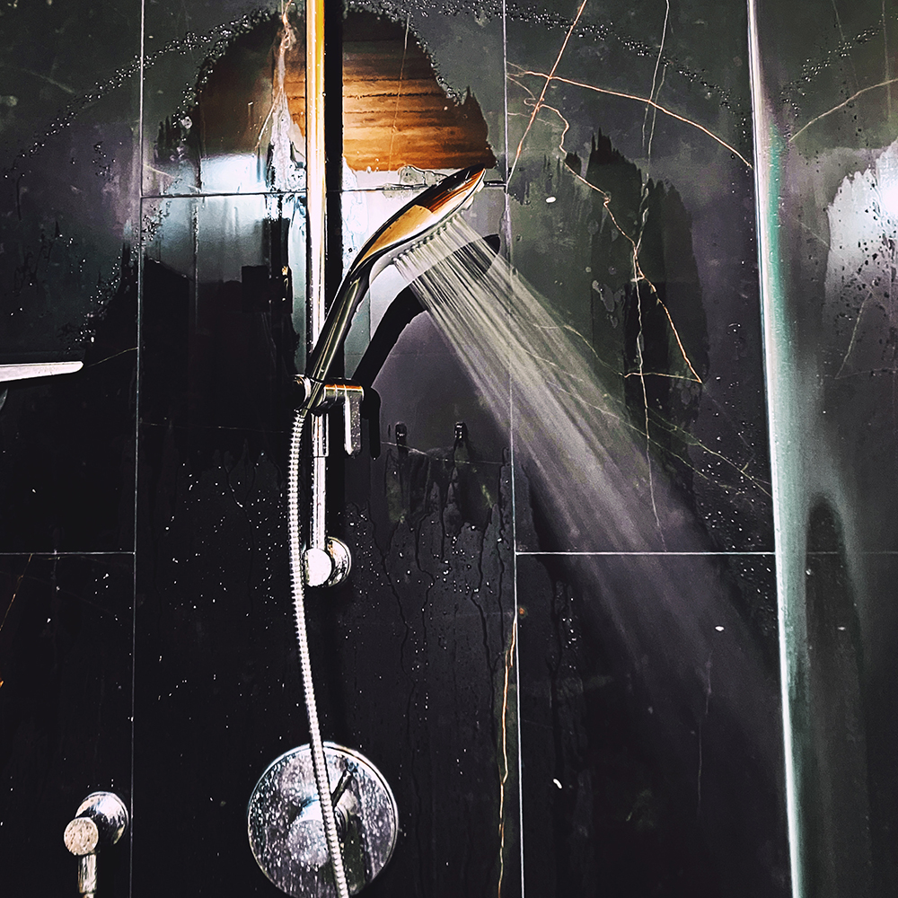 Photograph of chrome shower head running in a black tiled shower