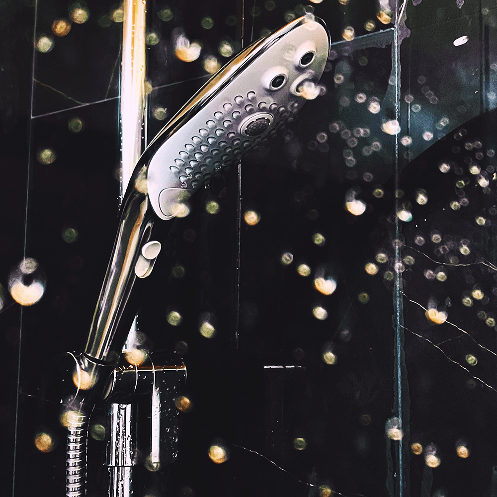 photograph through a wet shower glass wall showing white and chrome detachable shower head 