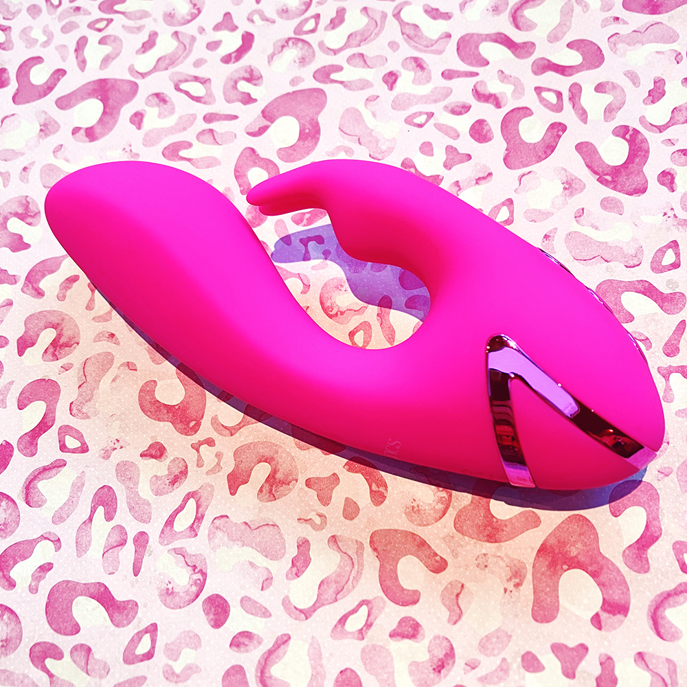 photograph of hot pink dual stimulator vibe lying on its side. clitoral arm has a distinct rabbit head silhouette