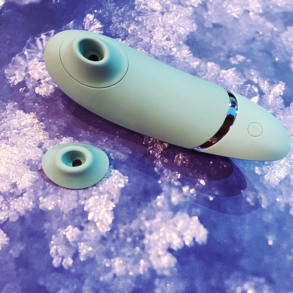Photograph of underside of mint-green oblong shaped clitoral Sex toy. Photo demonstrates size differences in two cone-shaped silicone nozzles that snap onto the toy